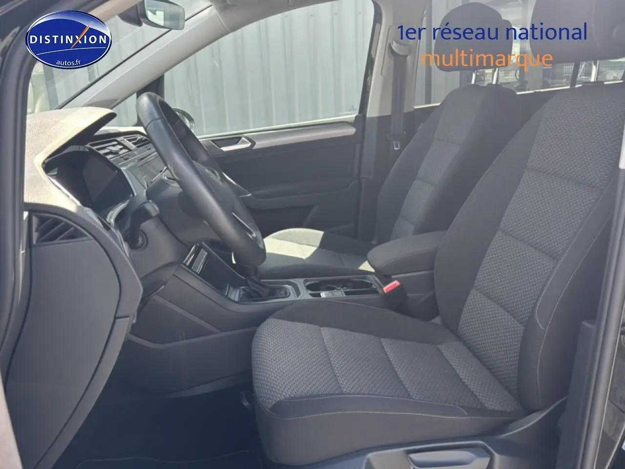 Vue intérieure côté conducteur du Volkswagen Touran 2025, sièges tissu gris et volant cuir multifonction.