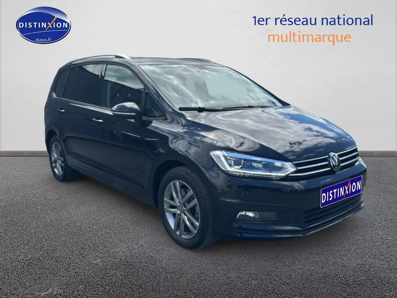 Volkswagen Touran noir 2025 en 3/4 avant droit, avec jantes alu et barres de toit visibles.