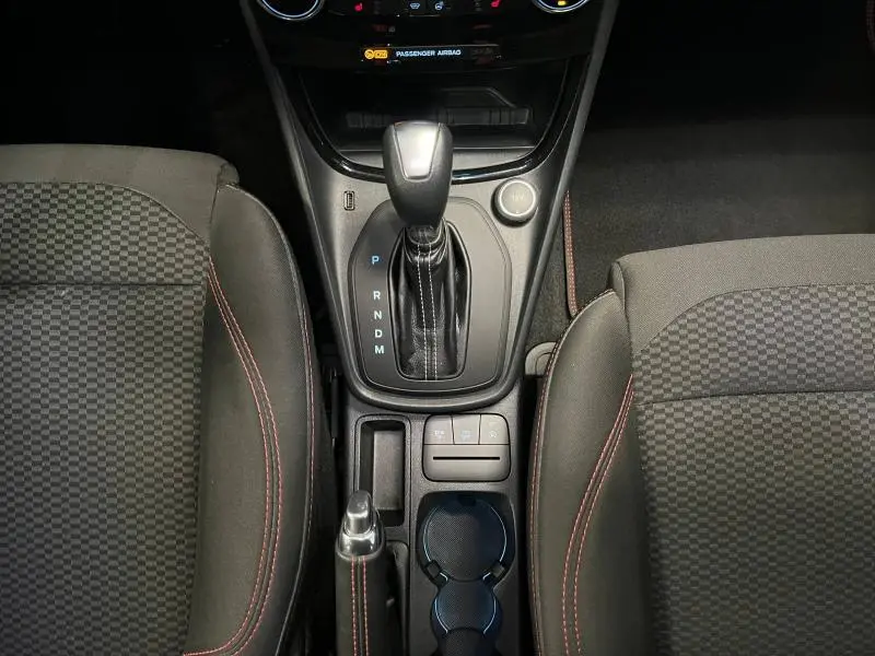 Vue plongeante sur la console centrale et levier de vitesses automatique du Ford Puma gris avec sièges sport noirs à surpiqûres rouges.