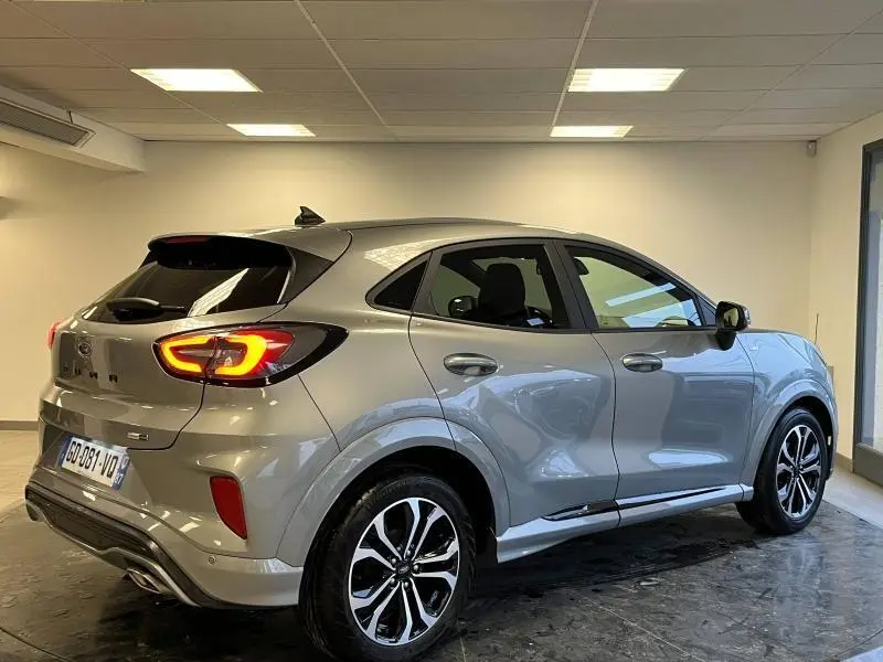 Ford Puma gris Solar métallisée vue 3/4 arrière droit en intérieur avec feux arrière LED allumés et jantes alu noires.