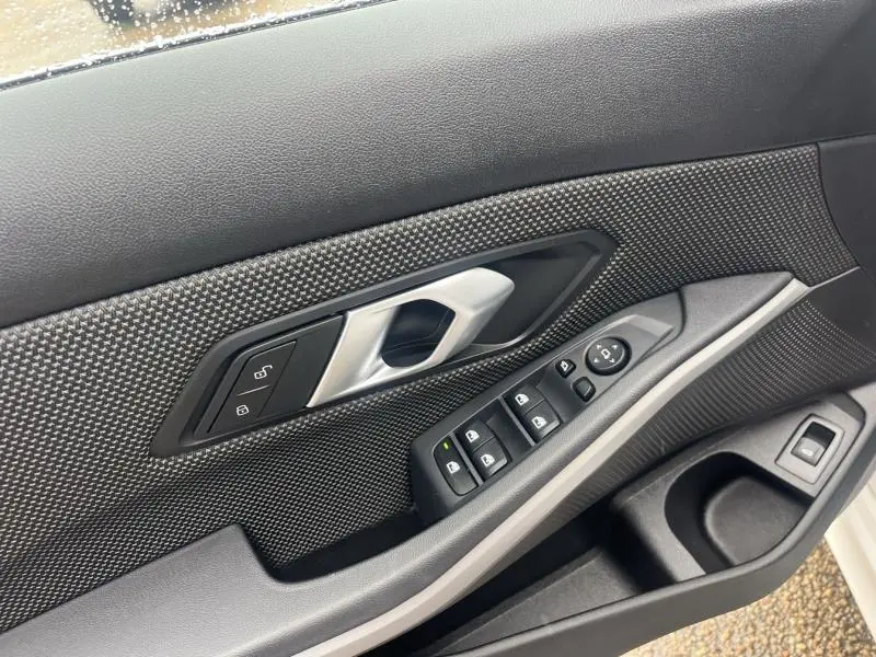 Détail de la porte côté conducteur de la BMW Série 3 316dA 2021 en Alpinweiss, avec commandes électriques et poignée argentée.