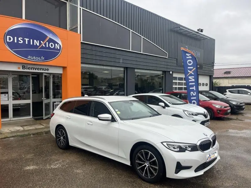 BMW Série 3 Touring 316dA blanche vue de trois quarts avant droit devant un concessionnaire Distinxion