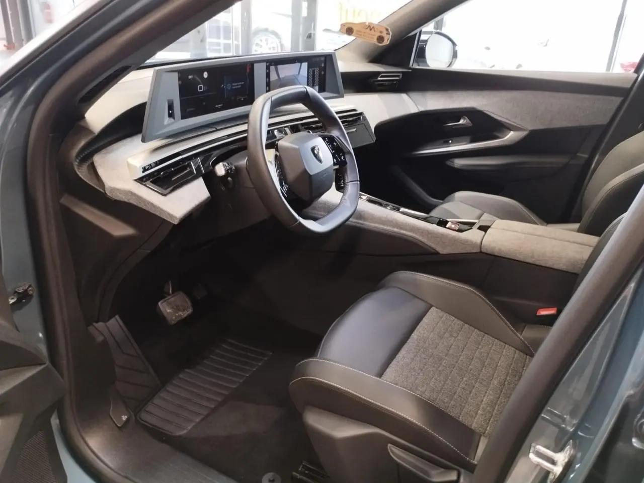 Vue intérieure côté conducteur du Peugeot 5008 2025, avec tableau de bord numérique et sellerie tissu gris et cuir noir.