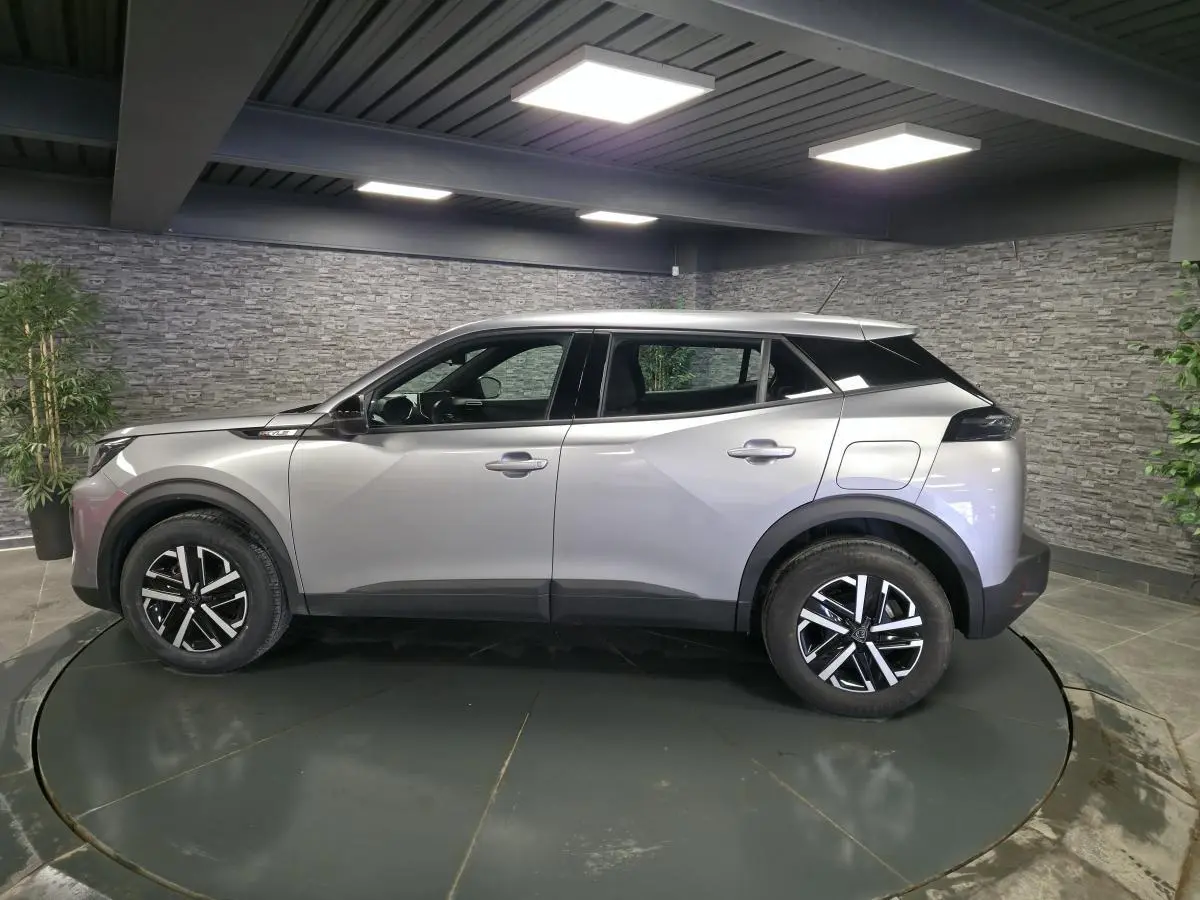 Peugeot 2008 gris en profil droit, jantes noires et argent, toit noir contrastant, dans un showroom intérieur.