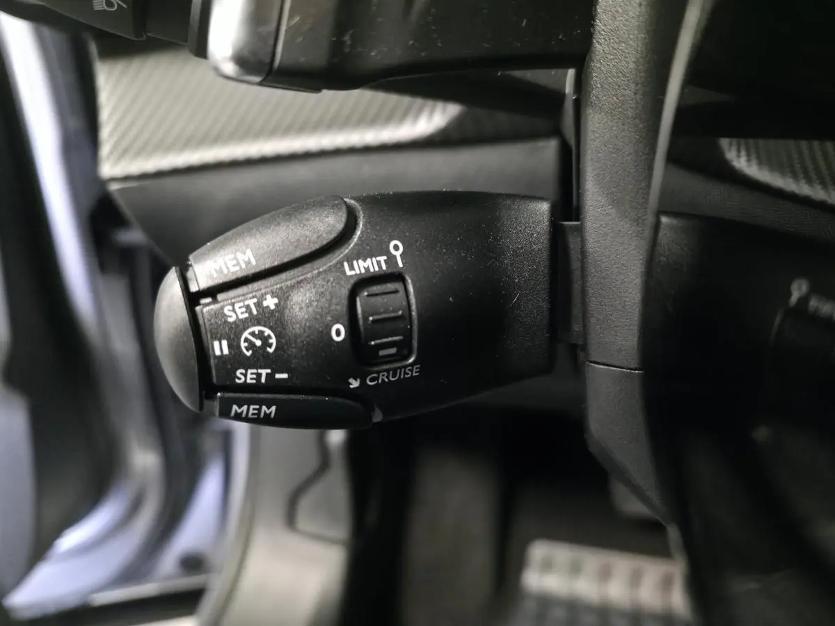 Gros plan sur la commande de régulateur de vitesse noire dans l'habitacle du Peugeot 2008 gris 2025.