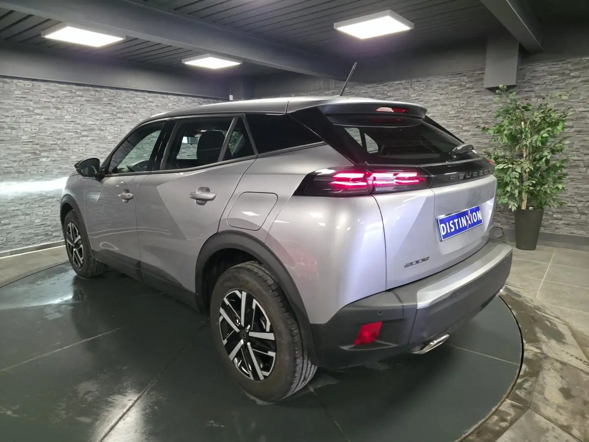 Peugeot 2008 gris métallisé vue 3/4 arrière droit, feux LED allumés et jantes noires avec inserts argentés.
