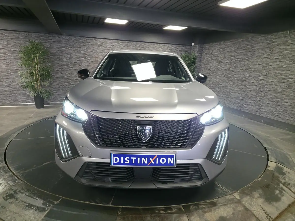 Vue de face du Peugeot 2008 gris avec calandre noire et feux LED allumés dans un showroom.