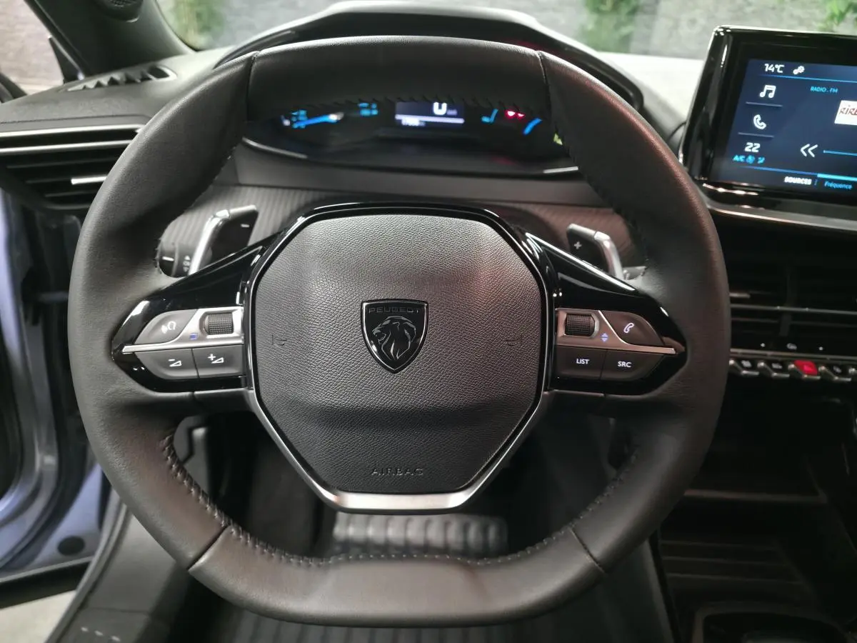 Vue rapprochée du volant cuir noir avec commandes intégrées du Peugeot 2008 gris, tableau de bord et écran tactile visibles.