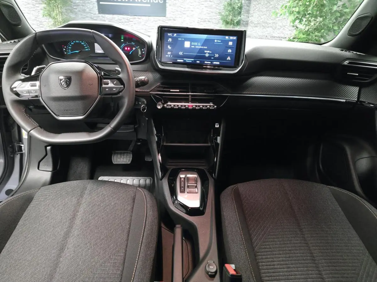 Vue intérieure avant du Peugeot 2008 gris 2025, tableau de bord carbone, écran tactile 10 pouces et volant compact cuir.