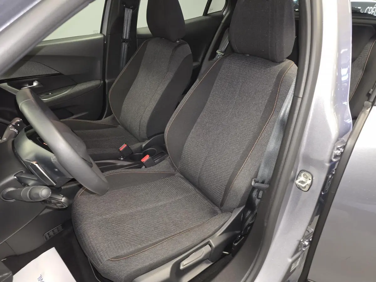 Vue intérieure côté conducteur du Peugeot 2008 gris 2025, sièges tissu gris chiné avec surpiqûres orange.