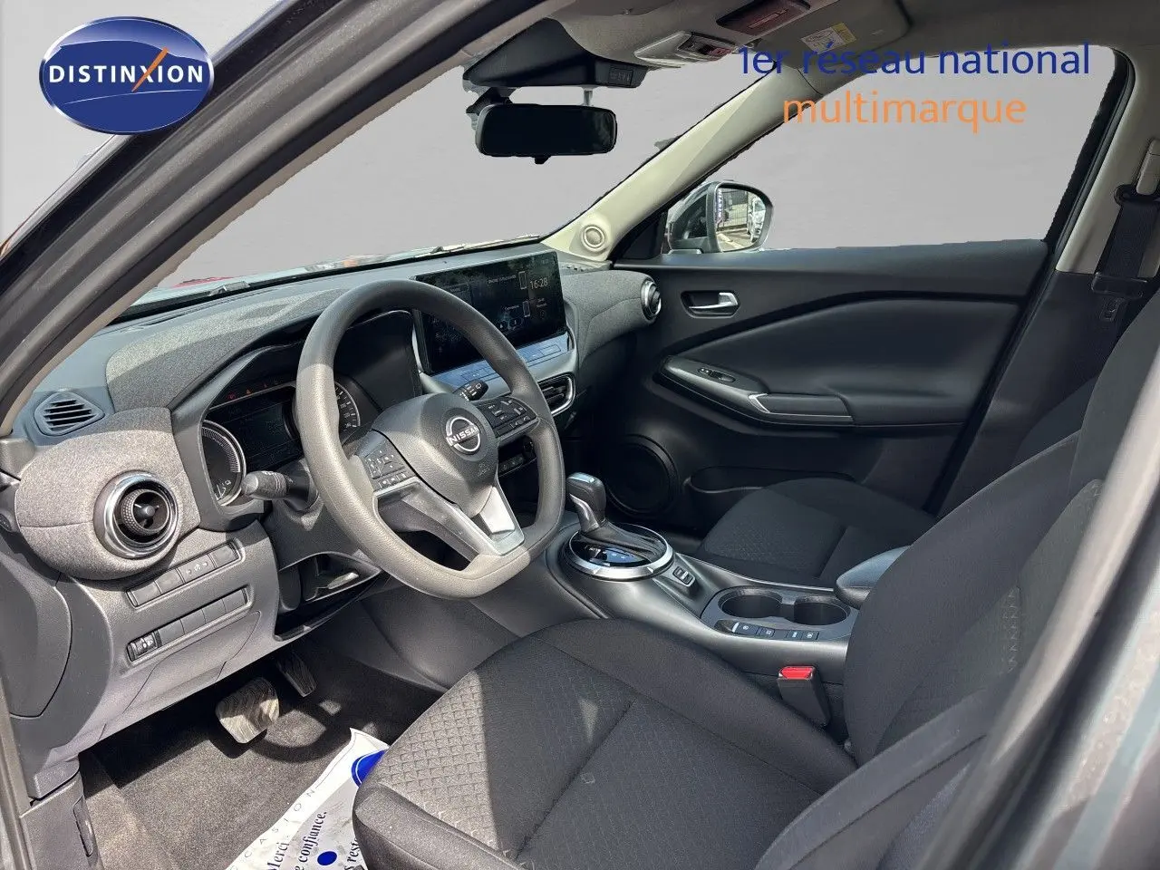 Vue intérieure côté conducteur du Nissan Juke Hybrid 2024, avec tableau de bord moderne et sièges tissu noir.