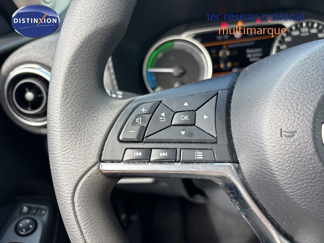 Gros plan sur les commandes au volant noir du Nissan Juke Hybrid 2024, avec tableau de bord et aérateur circulaire en arrière-plan.