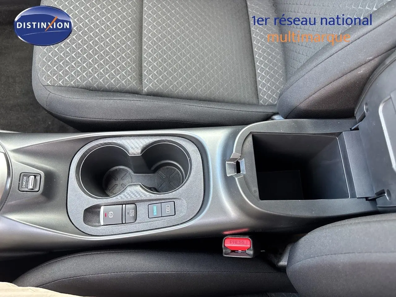 Vue plongeante sur la console centrale du Nissan Juke Hybrid 2024, avec porte-gobelets et accoudoir ouvert en tissu noir.