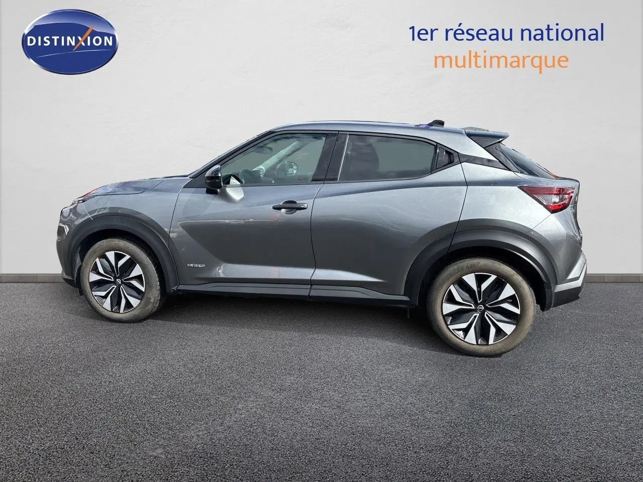 Nissan Juke Hybrid gris squale métal vu de profil côté gauche, avec jantes alliage et lignes dynamiques marquées.