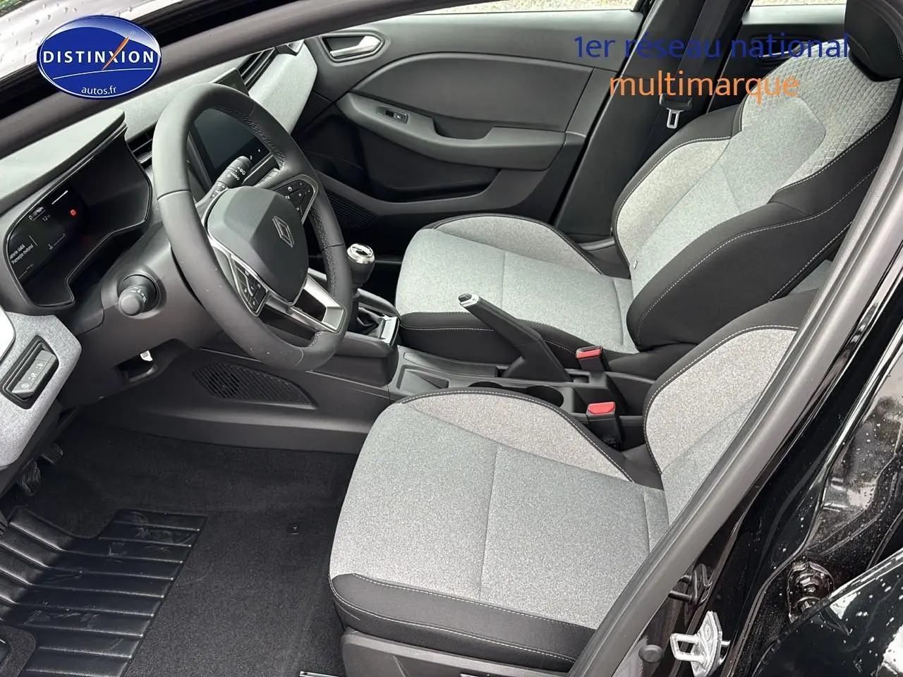 Intérieur avant droit de Renault Clio V noir 2025, sièges gris clair et volant multifonction visible.