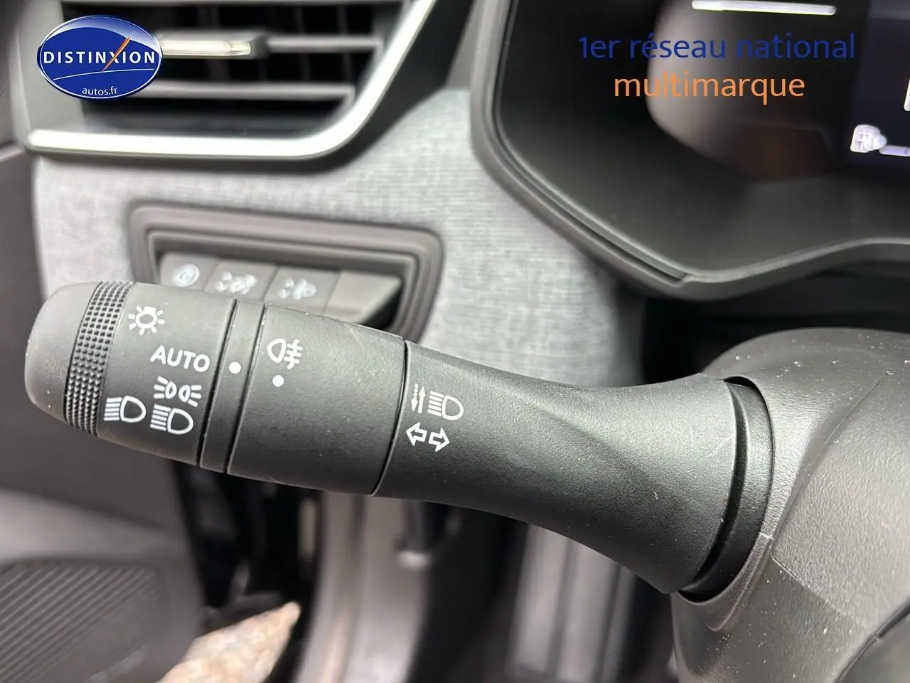 Gros plan sur la manette de commande des phares et clignotants dans l'habitacle d'une Renault Clio V noire.