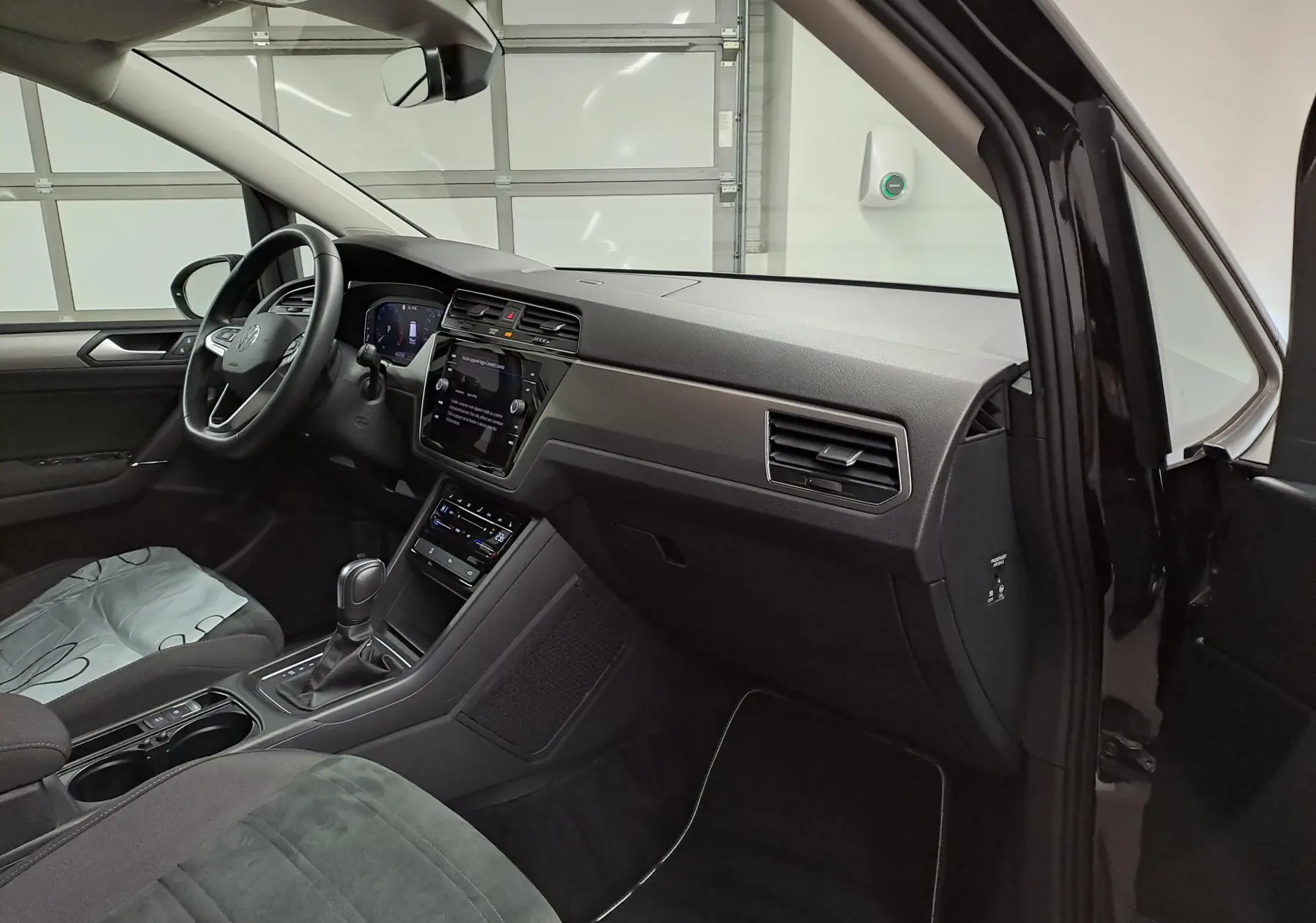 Vue intérieure côté conducteur du Volkswagen Touran 2025 noir grenadille, avec sellerie Alcantara et tableau de bord moderne.