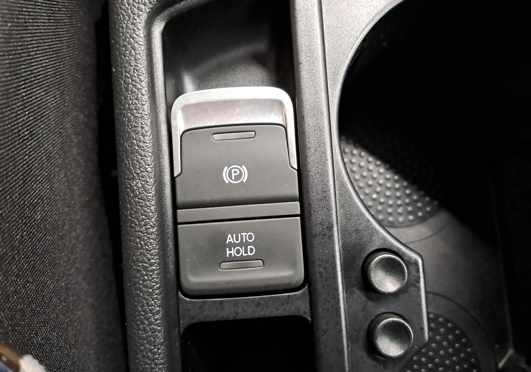 Gros plan sur la console centrale du Volkswagen Touran 2025, montrant les boutons de frein de parking électronique et Auto Hold.