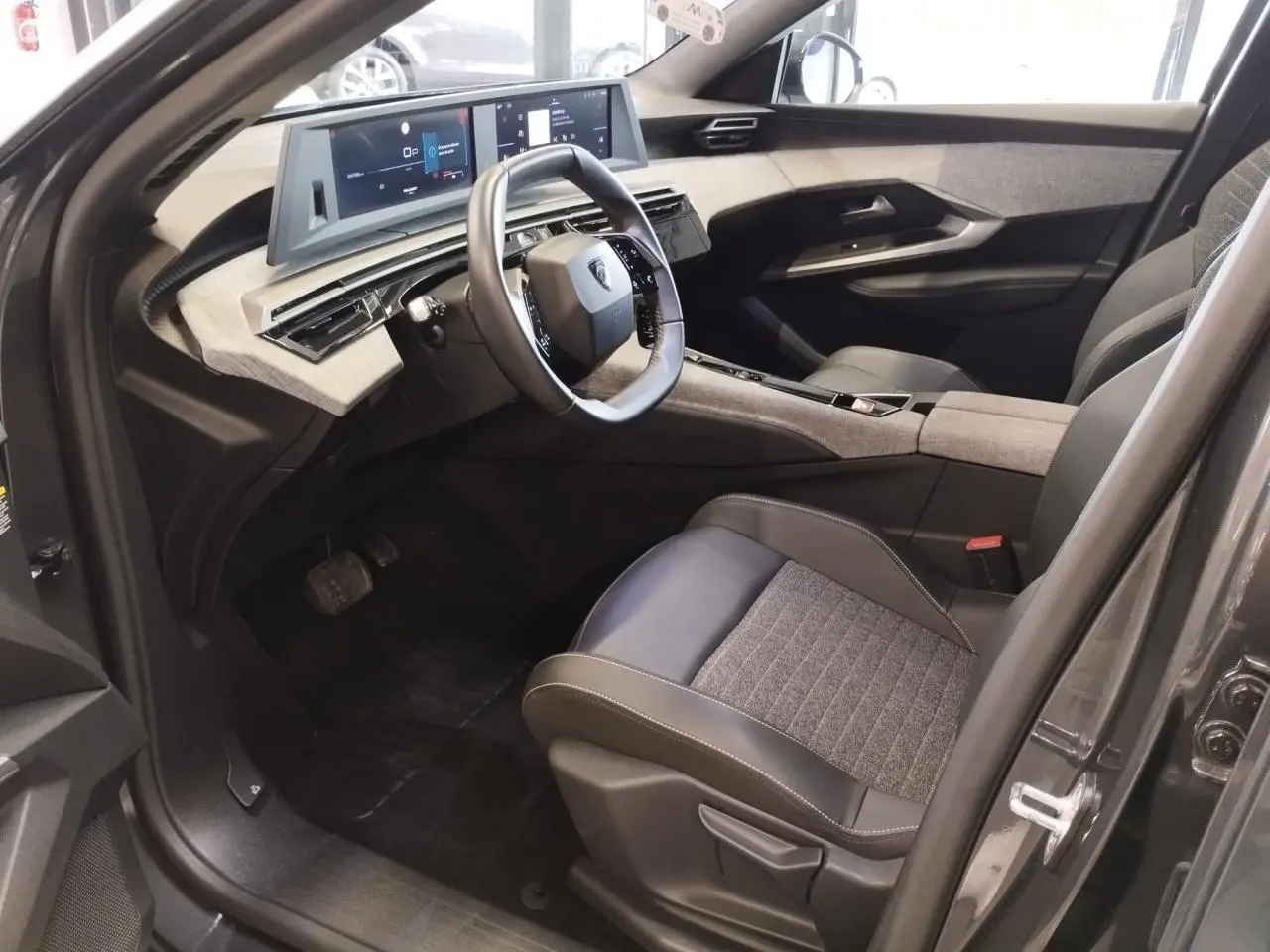 Intérieur avant droit du Peugeot 5008 gris titanium 2025, volant compact, tableau de bord numérique et sellerie tissu cuir.
