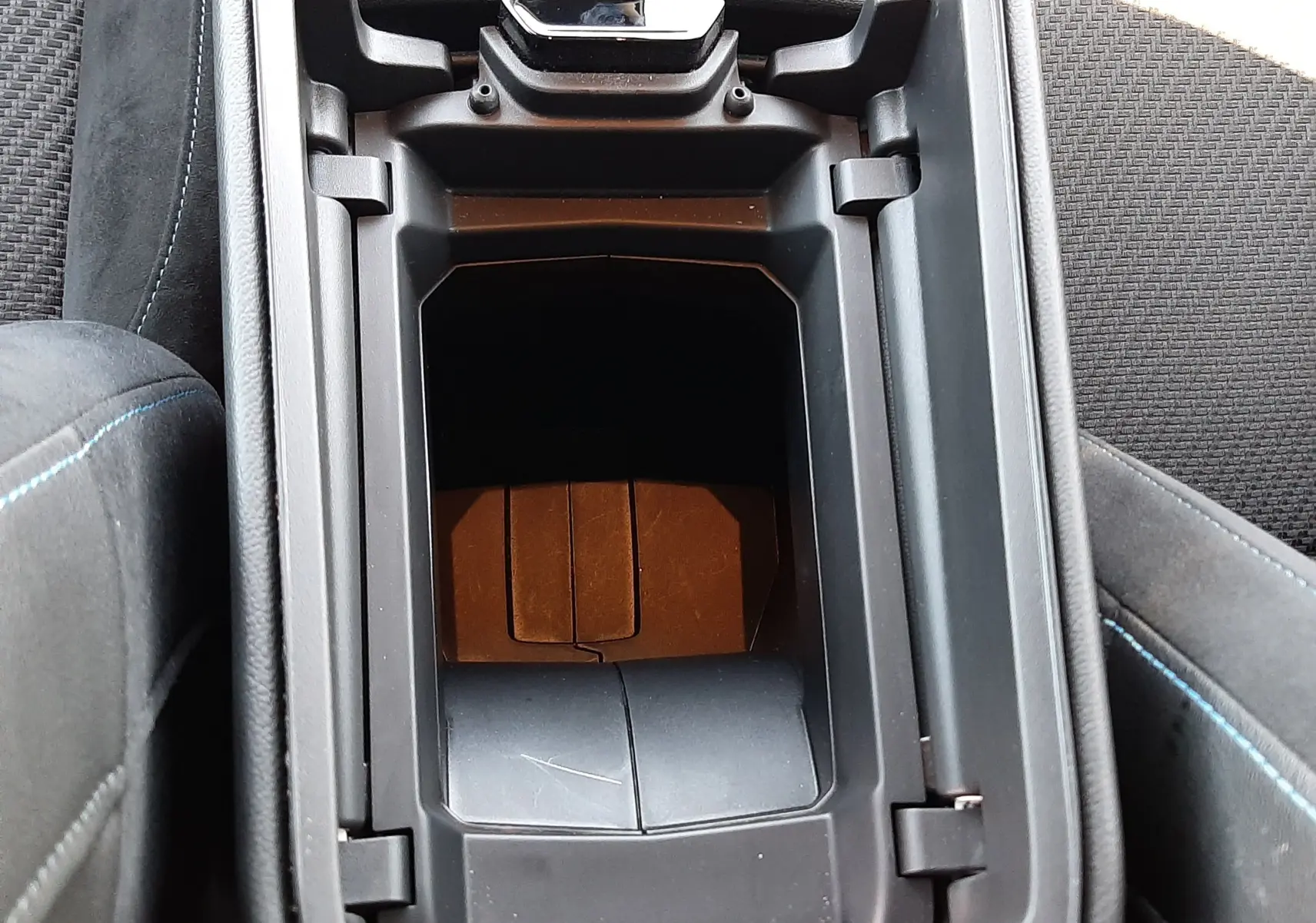 Vue plongeante sur le rangement central noir de l’habitacle du Renault Austral E-Tech hybride 2025, avec surpiqûres bleues.