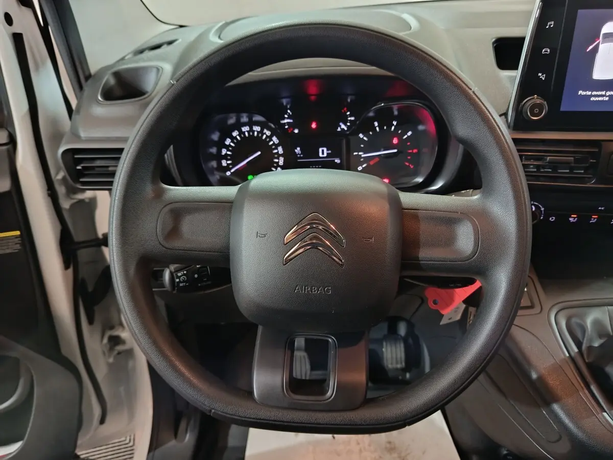 Vue rapprochée du volant noir avec logo Citroën et tableau de bord éclairé du Berlingo blanc 2021.