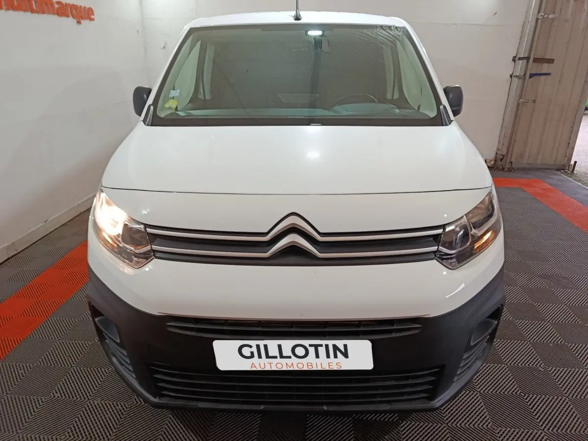 Vue avant d’un Citroën Berlingo blanc 2021 avec phares allumés et pare-chocs noir dans un garage.