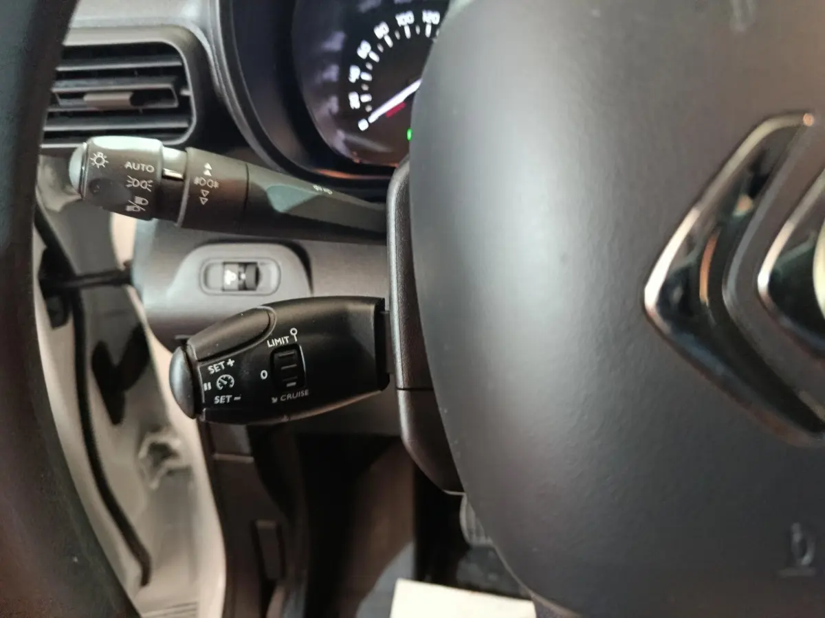 Vue rapprochée du volant et des commandes de régulateur de vitesse du Citroën Berlingo blanc, côté gauche.