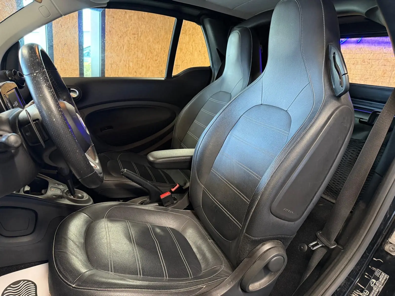 Vue intérieure côté conducteur de la Smart Fortwo Cabrio noire 2019, sièges semi-cuir et volant multifonctions visibles.