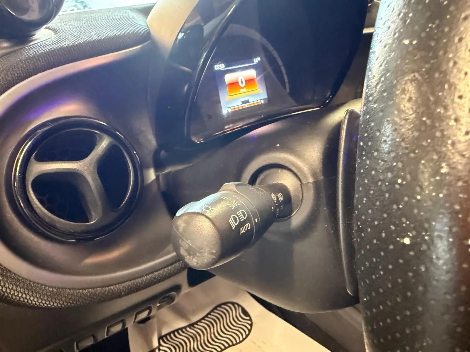 Gros plan sur la commande des phares et le tableau de bord numérique d'une Smart Fortwo Cabrio noir, intérieur semi-cuir.