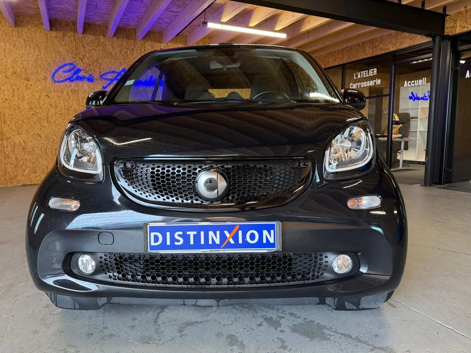 Vue frontale d'une Smart Fortwo Cabrio noire 2019 avec calandre noire et phares arrondis, en intérieur showroom.