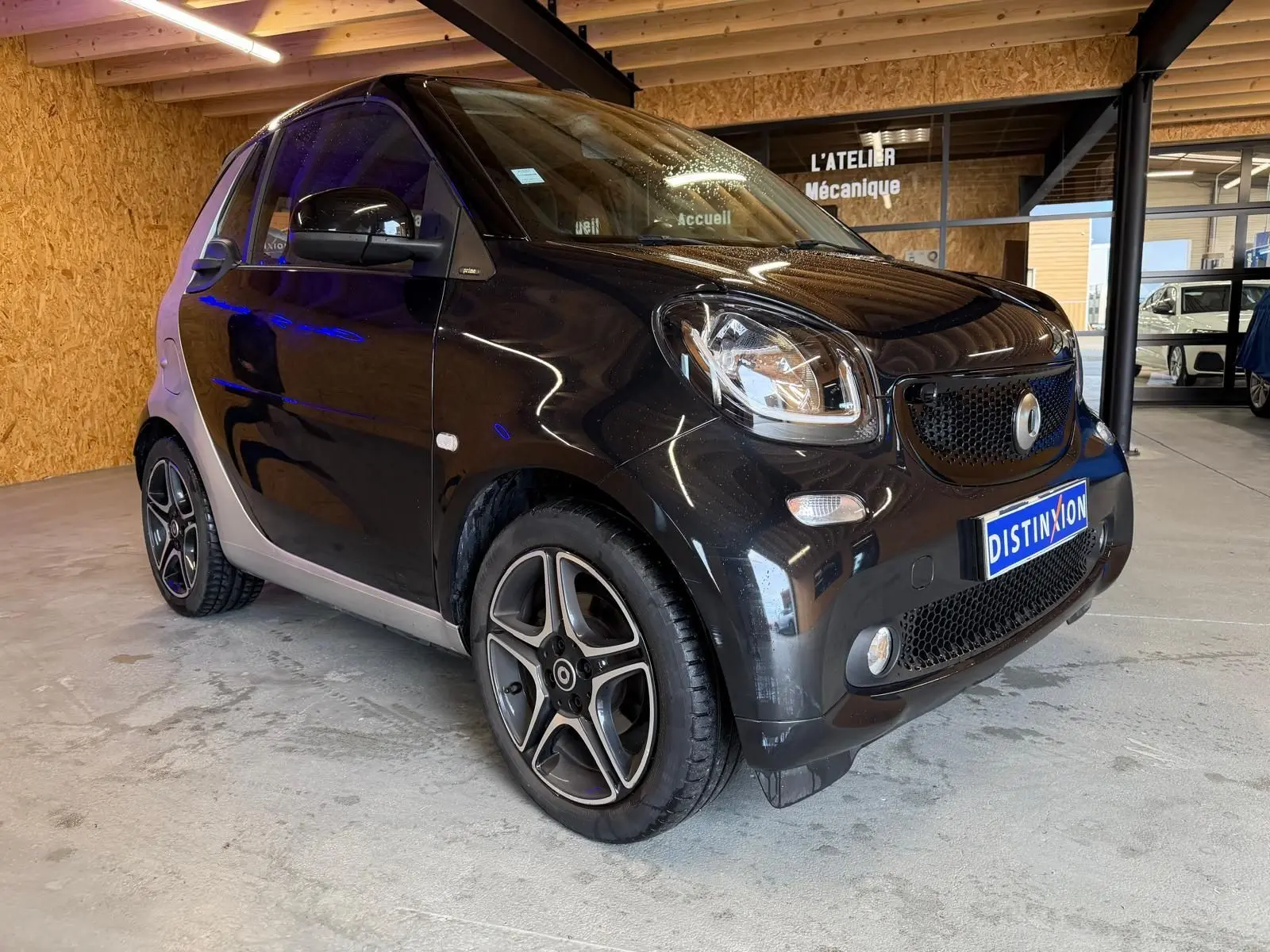 Vue 3/4 avant droite d'une Smart Fortwo Cabrio noire avec jantes alu 16'' et toit ouvrant électrique en intérieur showroom.