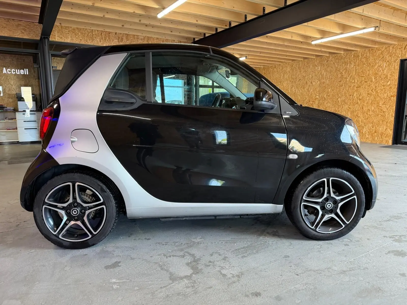 Vue de profil côté gauche d'une Smart Fortwo Cabrio noire avec toit ouvert et jantes alu 16 pouces bicolores.