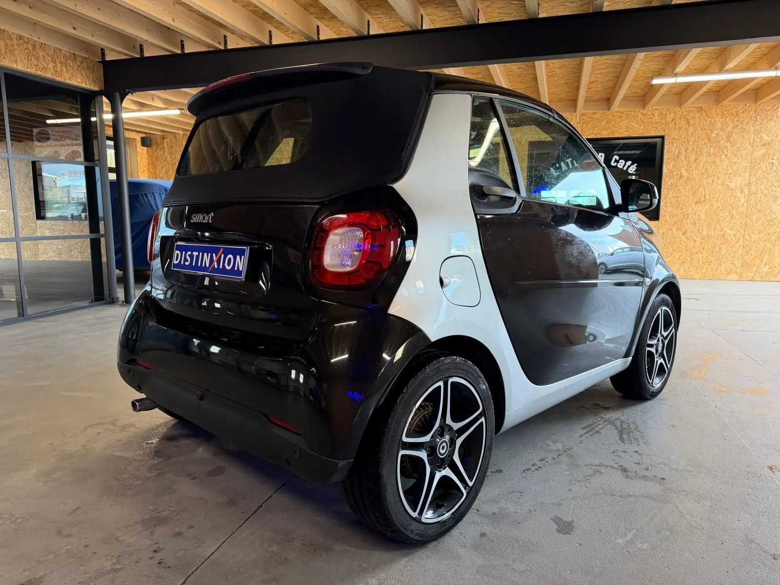 Vue 3/4 arrière droite d'une Smart Fortwo Cabrio noire avec toit souple et jantes alu 16 pouces dans un garage.