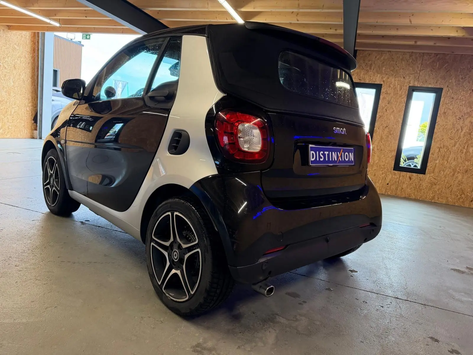Vue 3/4 arrière droite d'une Smart Fortwo Cabrio noire avec jantes alu 16'' dans un garage lumineux.