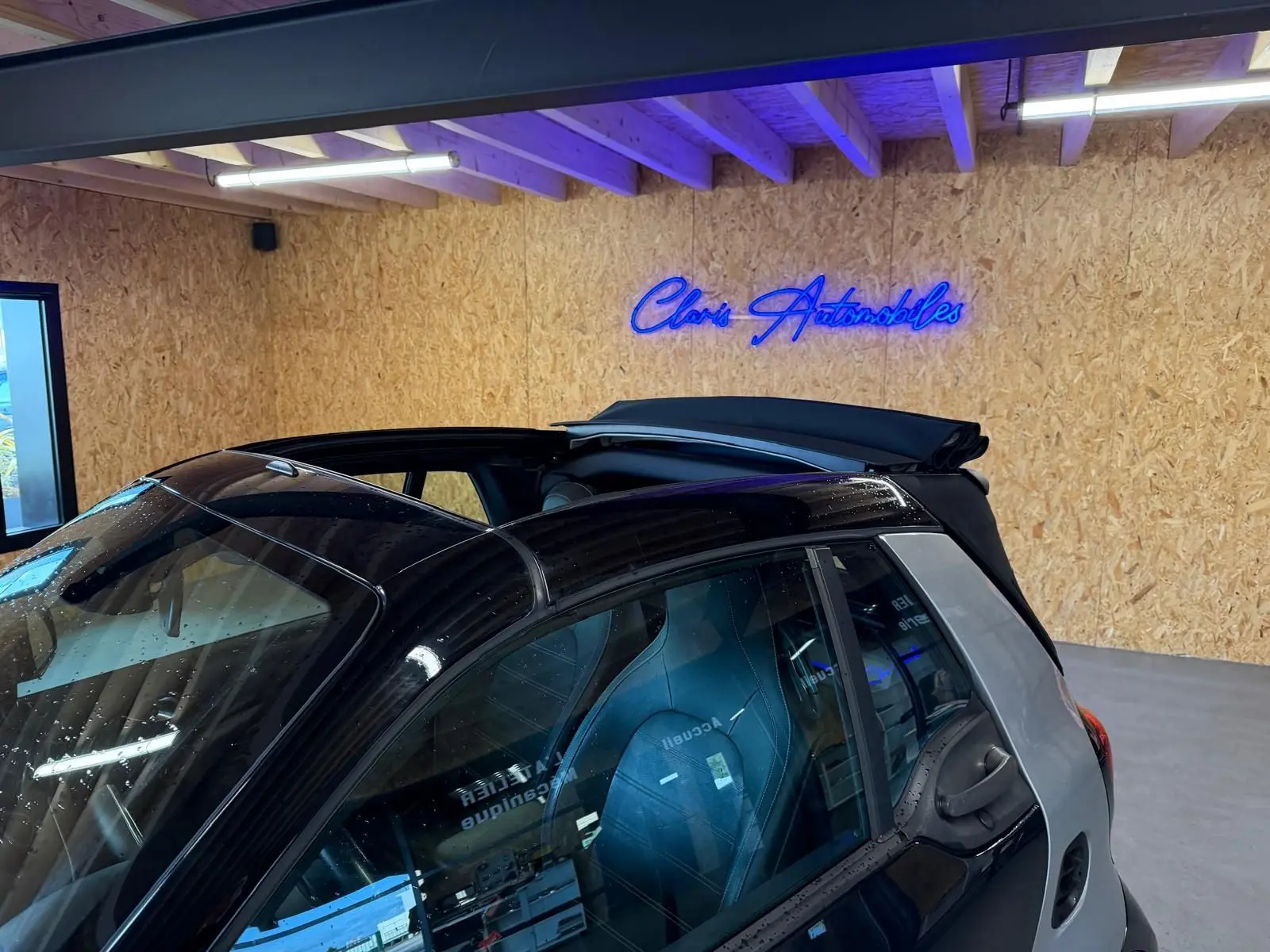 Vue 3/4 arrière droite d'une Smart Fortwo Cabrio noire avec toit ouvrant électrique partiellement ouvert en intérieur showroom.