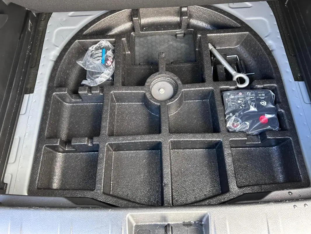 Vue plongeante sur le rangement noir sous le coffre du Jeep Renegade bleu foncé, avec outils et compresseur visibles.