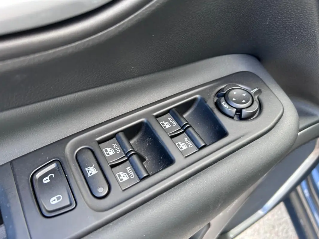 Gros plan sur les commandes de vitres électriques et rétroviseurs sur la porte côté conducteur du Jeep Renegade bleu foncé.