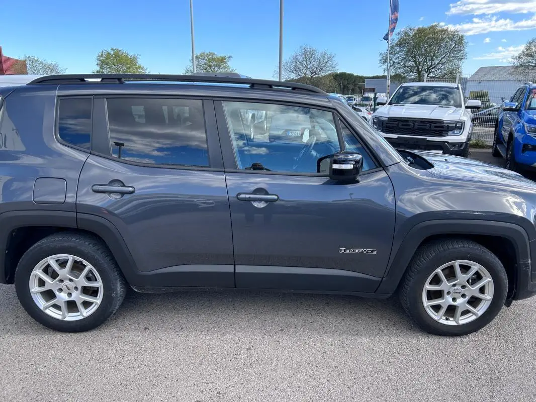 Jeep Renegade bleu foncé vu de profil côté gauche, avec jantes alliage 17 pouces et barres de toit noires.