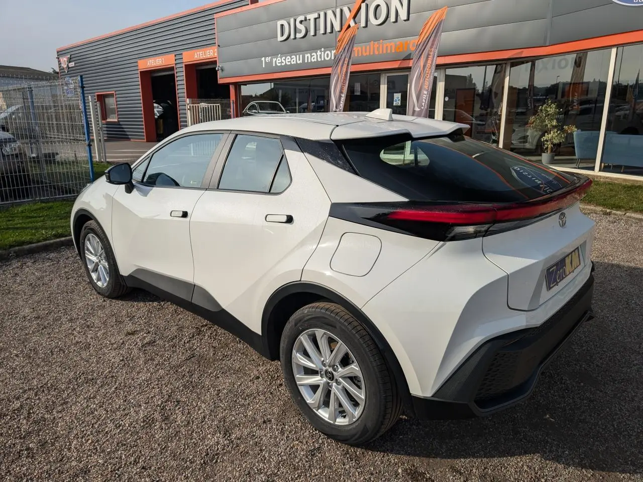 Toyota C-HR 1.8 Hybrid blanc vu en 3/4 arrière droit, avec feux arrière étirés et toit noir contrastant.