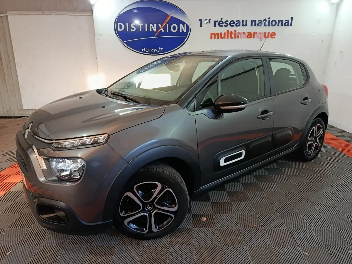 Citroën C3 BlueHDi 100 gris foncé vue 3/4 avant droit avec protections latérales blanches et jantes stylisées.