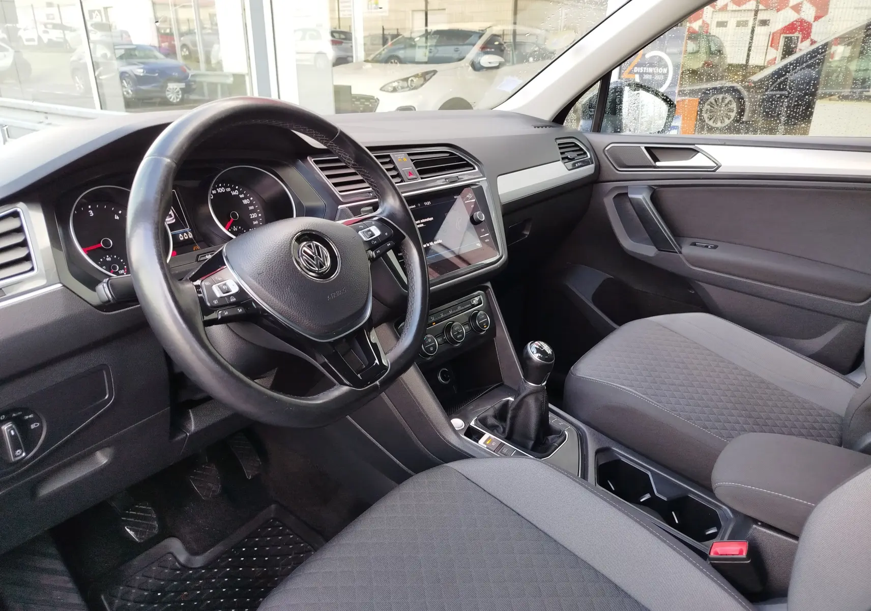 Vue intérieure côté conducteur du Volkswagen Tiguan 2019, tableau de bord noir avec volant cuir et boîte manuelle.