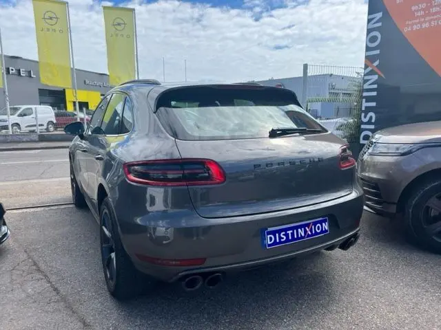 Vue 3/4 arrière d'un Porsche Macan gris 2015 avec double sortie d'échappement et feux arrière allongés.