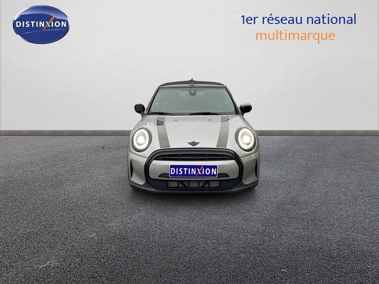 Vue frontale d'une MINI Cabriolet 2023 Melting Silver Metal avec bandes noires et phares allumés.