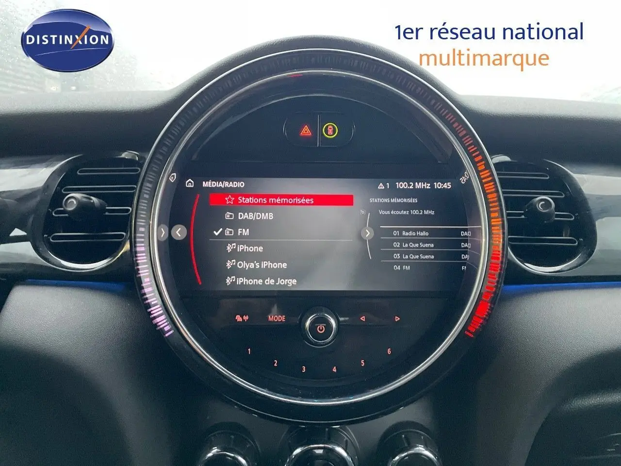 Affichage central circulaire du système multimédia de la MINI Cabriolet 2023, avec menu radio FM et connectivité iPhone visible.