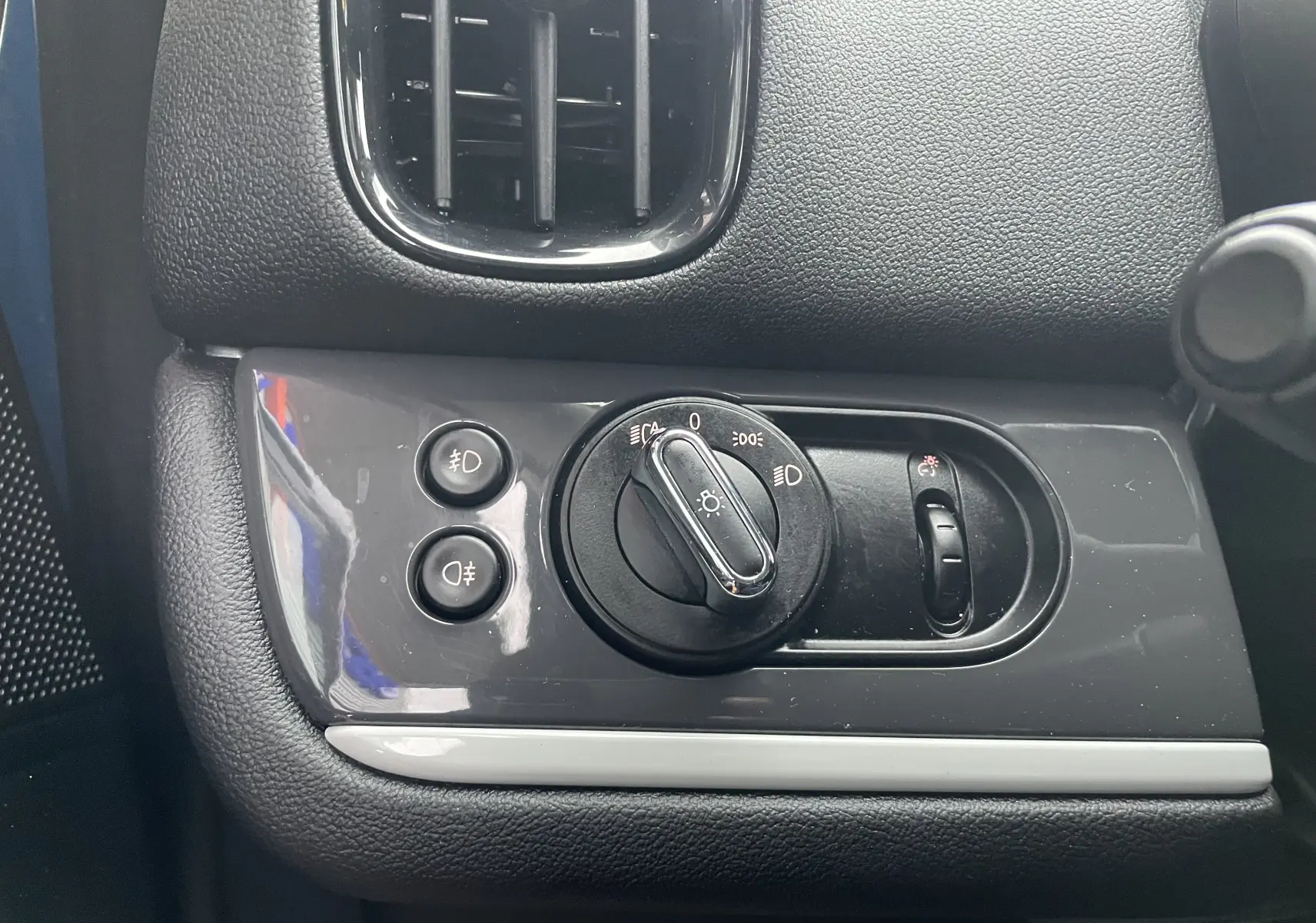 Détail du panneau de commande des phares noir brillant à gauche du tableau de bord du MINI Countryman bleu Island Metal.