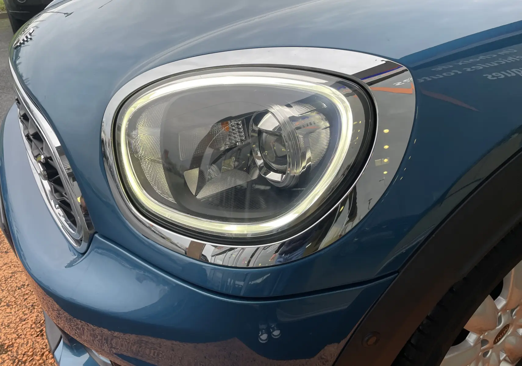 Gros plan sur le phare avant droit d'une MINI Countryman Cooper S bleu Island Metal avec détails chromés et calandre visible.