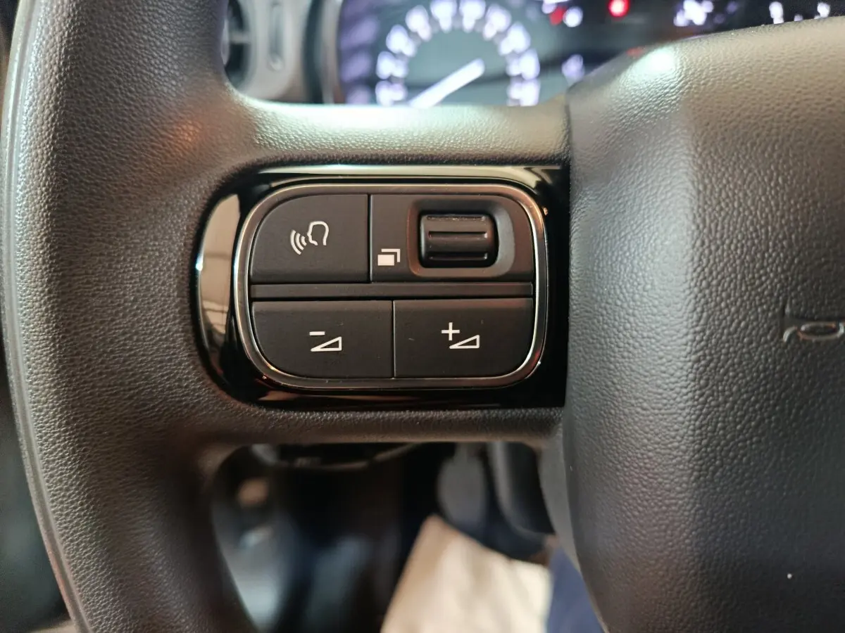 Gros plan sur les commandes multifonctions noires du volant de la Citroën C3 BlueHDi 100 BVM PLUS 2024.