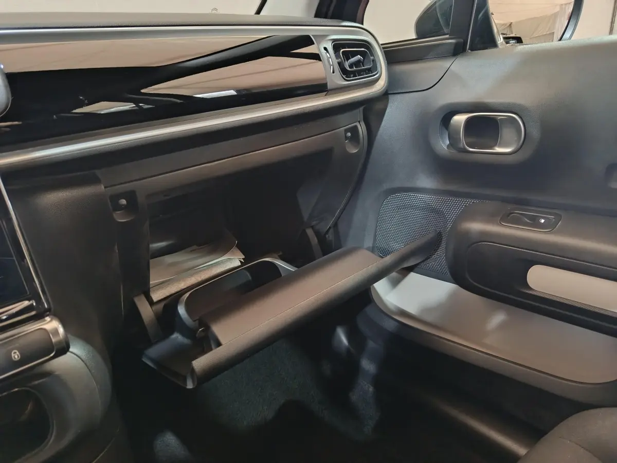 Vue intérieure côté passager de la Citroën C3 2024 noire, avec boîte à gants ouverte et tableau de bord noir brillant.