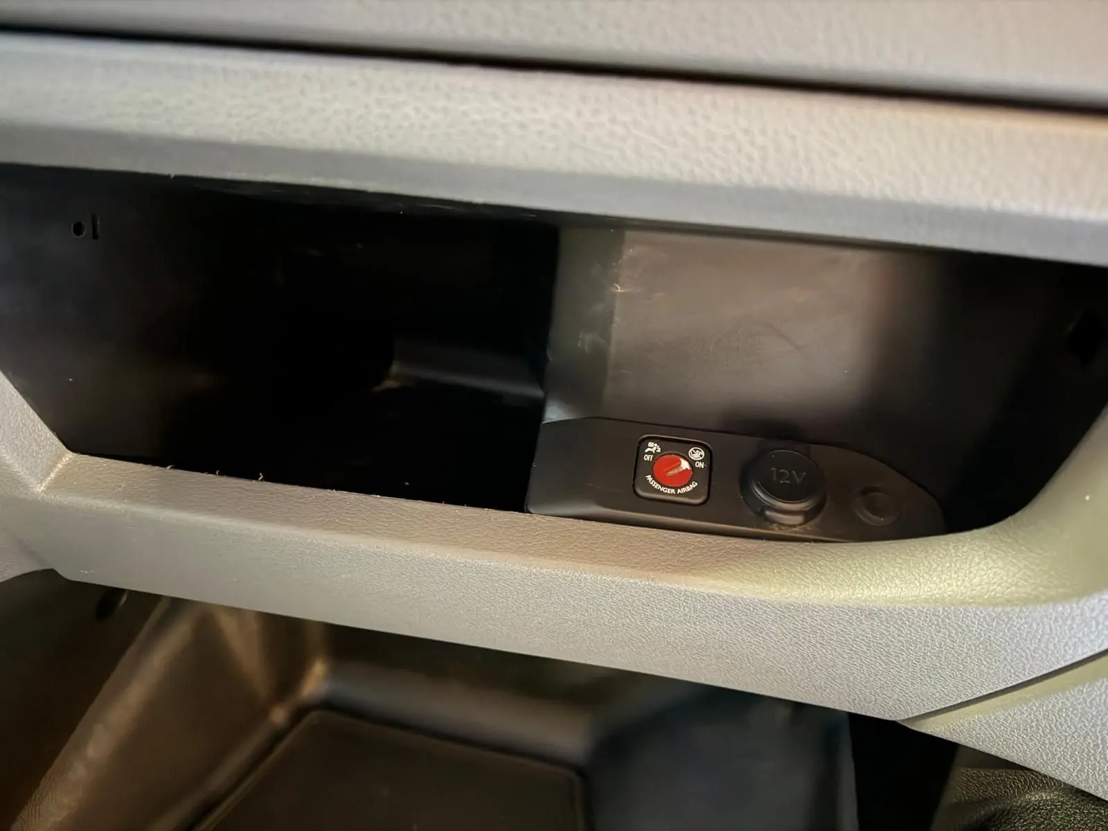 Gros plan sur la boîte à gants grise du Citroën Jumpy 2.0 BlueHDi 180, montrant un bouton de désactivation airbag et prise 12V.