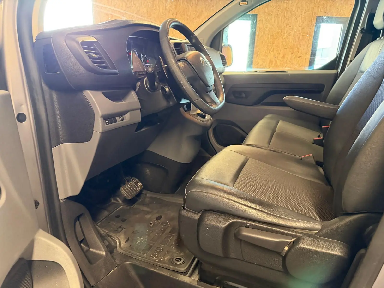 Vue intérieure côté conducteur du Citroën Jumpy gris 2022, montrant le volant, tableau de bord et sièges avant en tissu noir.